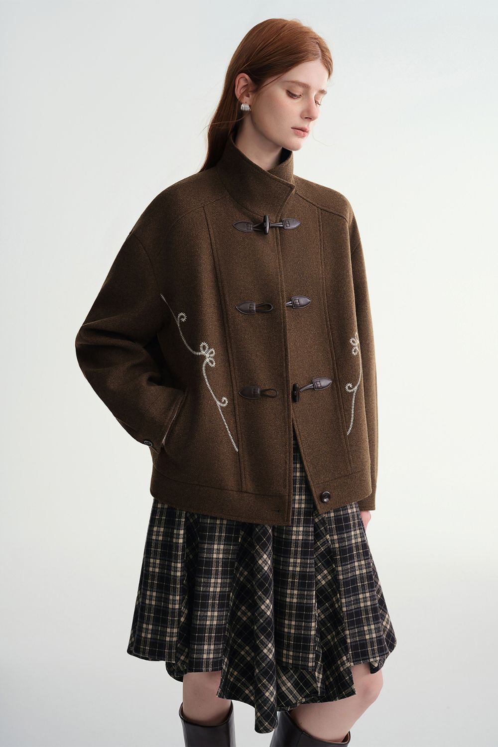 Model wearing a brown toggle jacket with a plaid skirt