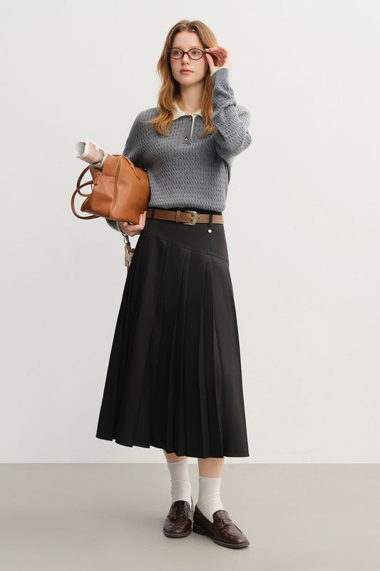 Model wearing a black pleated midi skirt with a belt and gray sweater, holding a brown bag