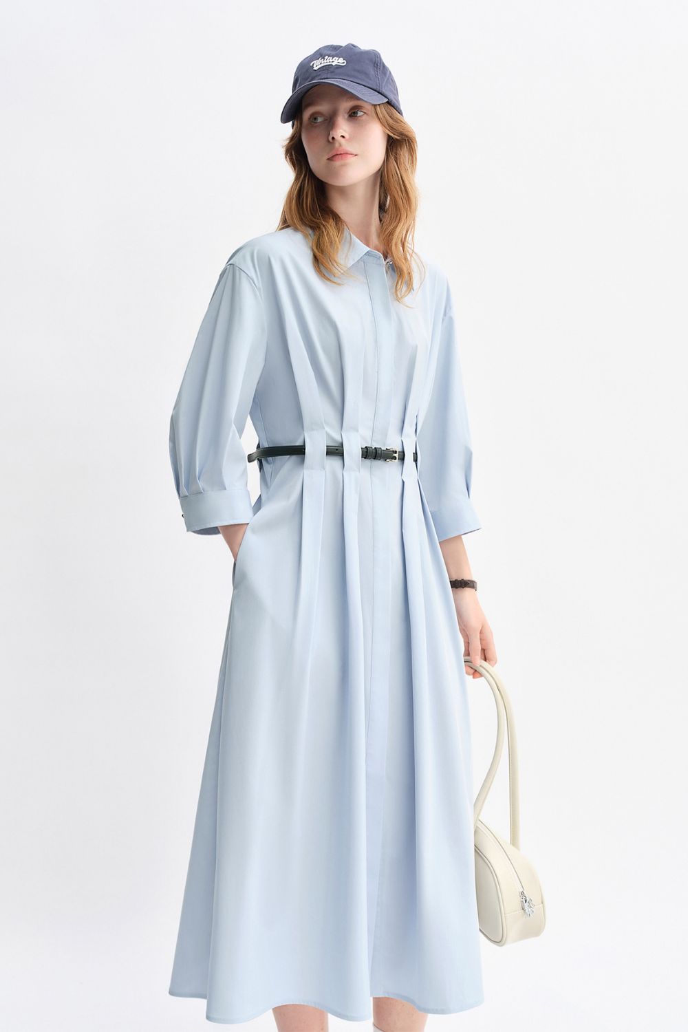 Model wearing a light blue belted midi dress with long sleeves and a casual cap