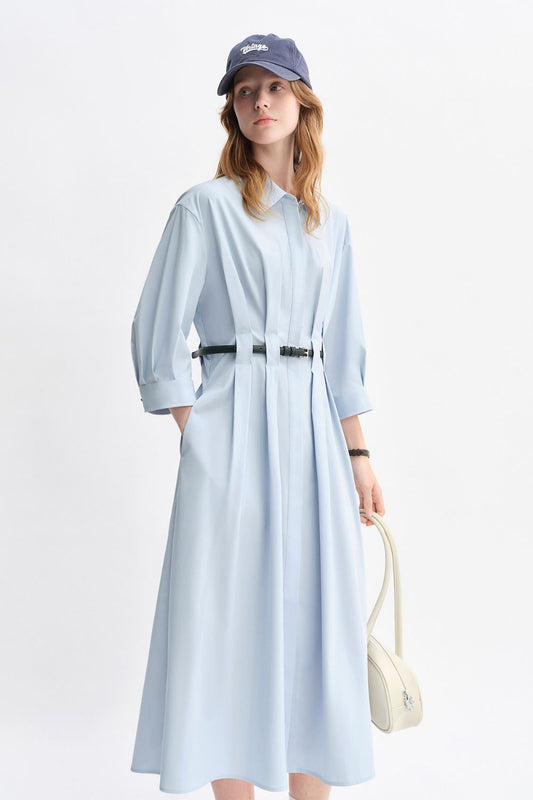 Model wearing a light blue belted midi dress with long sleeves and a casual cap