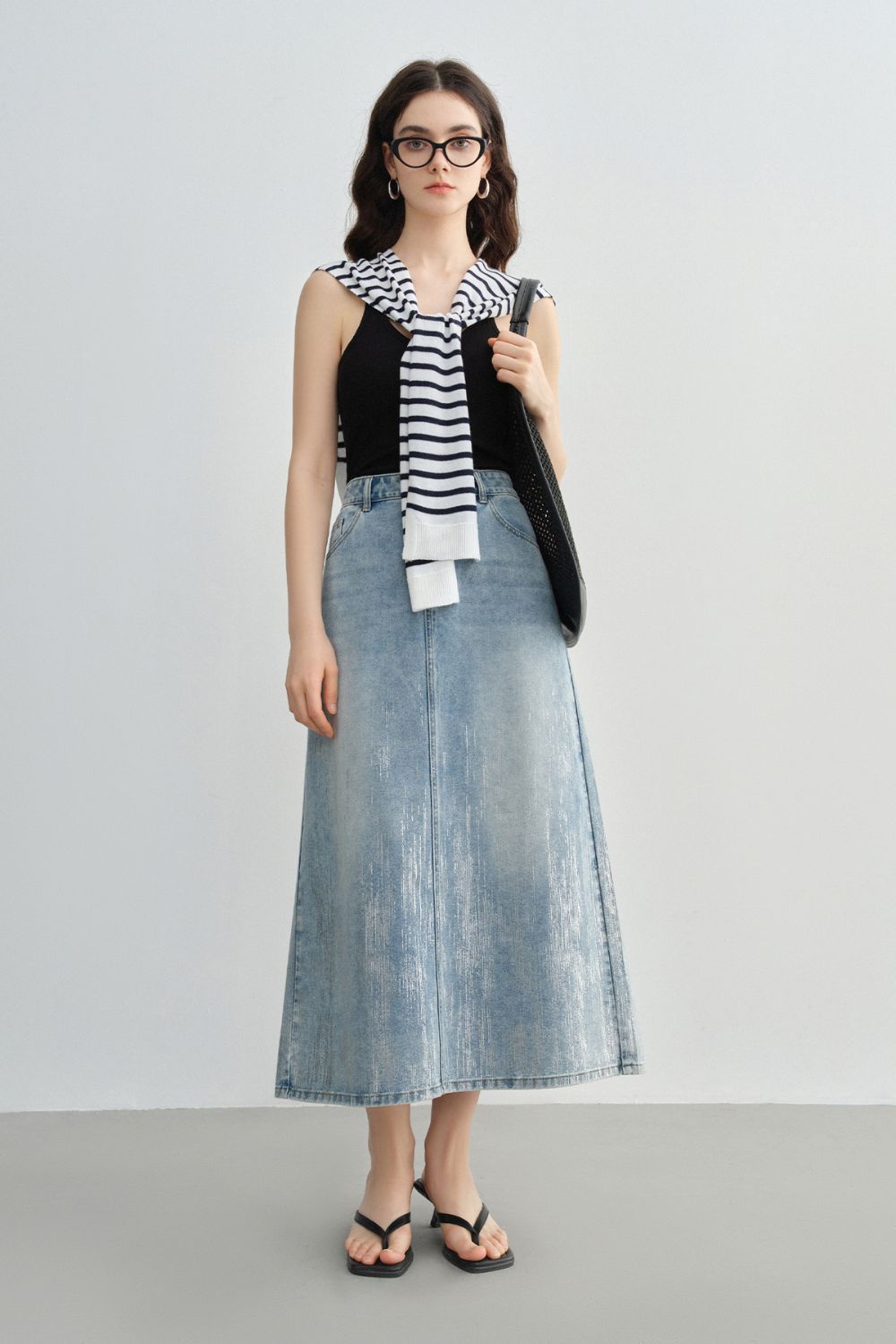 Model wearing a high-waisted light blue A-line denim skirt styled with a striped top and sandals