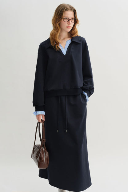 Model wearing a navy blue long-sleeve pullover with striped cuffs and a matching navy blue midi skirt