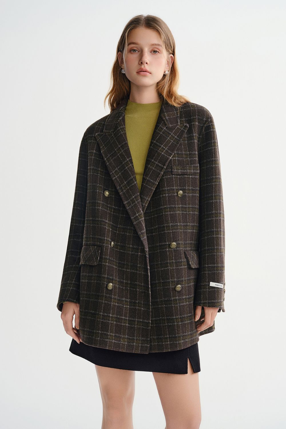 Model wearing a brown plaid double-breasted coat with a green top and black mini skirt