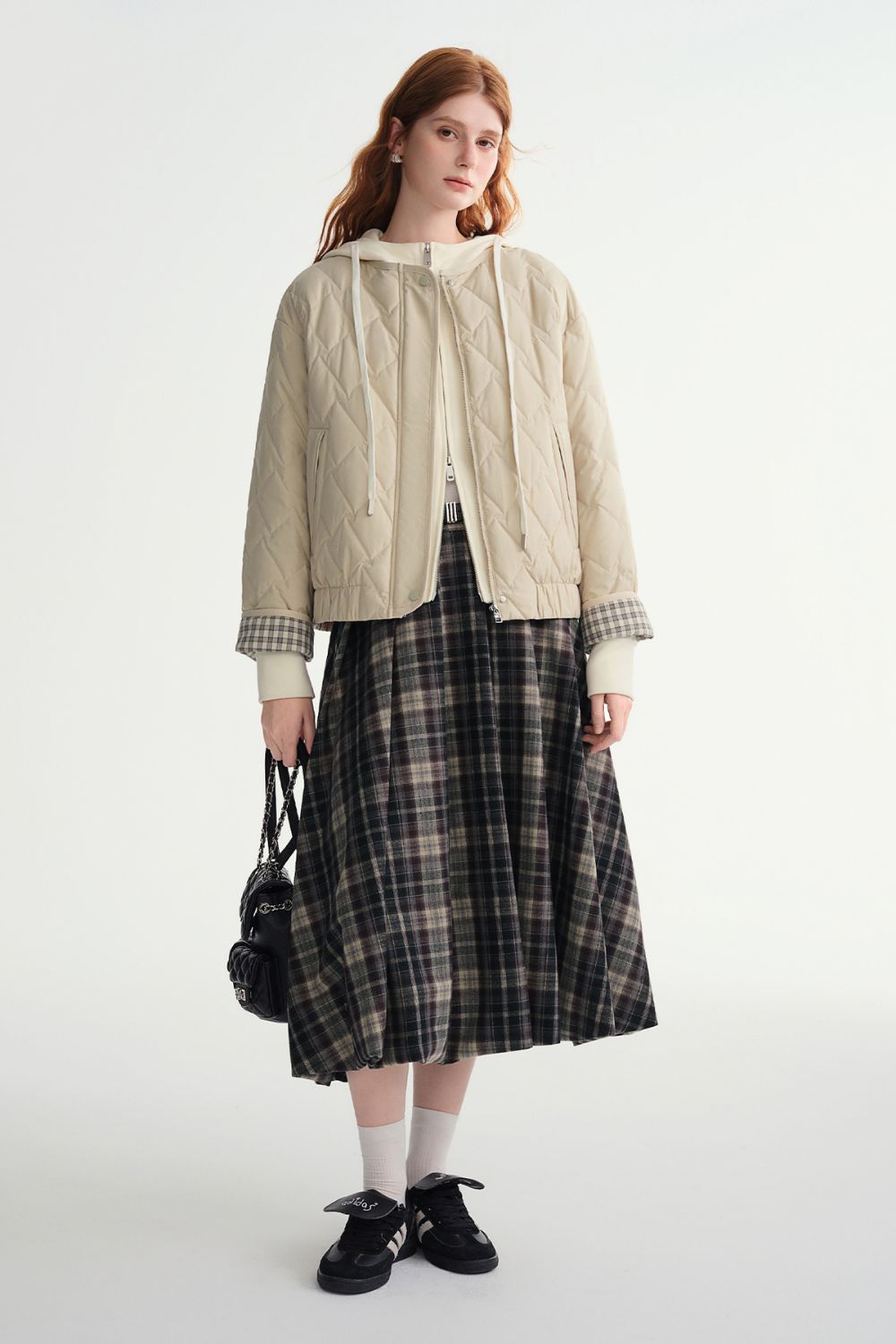 Front view of beige quilted jacket styled with plaid skirt and black handbag