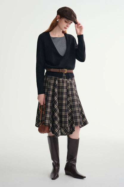 Model wearing a black and beige plaid A-line skirt styled with a black cardigan, gray top, and knee-high boots