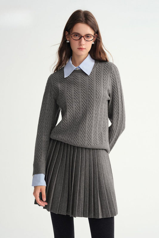 Model wearing gray cable-knit sweater layered over blue collared shirt with matching gray pleated skirt