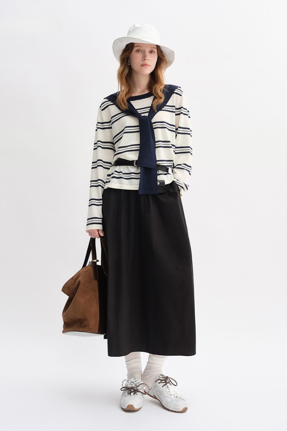 Model wearing striped long-sleeve top with navy collar and black maxi skirt, styled with white hat and tote bag