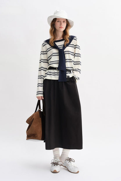 Model wearing striped long-sleeve top with navy collar and black maxi skirt, styled with white hat and tote bag