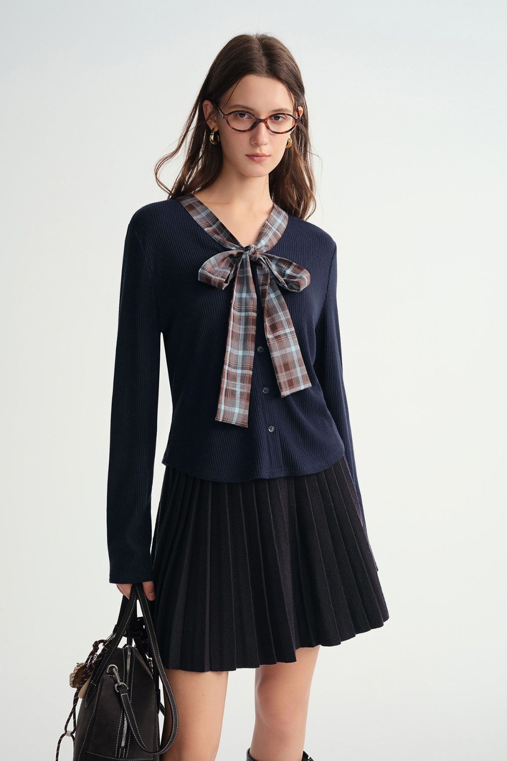 Model wearing a navy blue long-sleeve top with plaid bow tie and pleated mini skirt