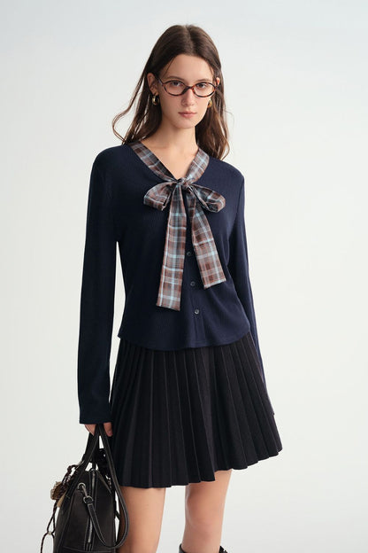 Model wearing a navy blue long-sleeve top with plaid bow tie and pleated mini skirt