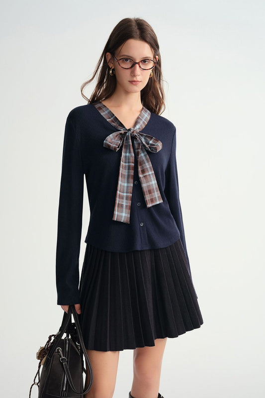 Model wearing a navy blue long-sleeve top with plaid bow tie and pleated mini skirt