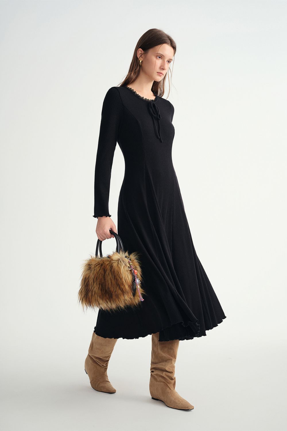 Model wearing long-sleeve black ribbed midi dress with ruffle trim and boots, holding a fur bag