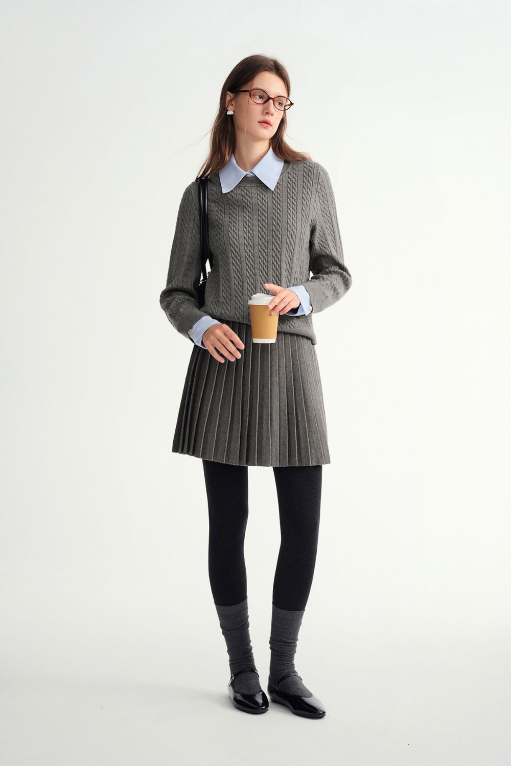 Full-body view of model in gray sweater and pleated skirt outfit