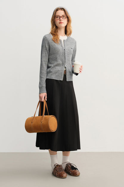 Model wearing black pleated midi skirt with gray sweater and brown bag