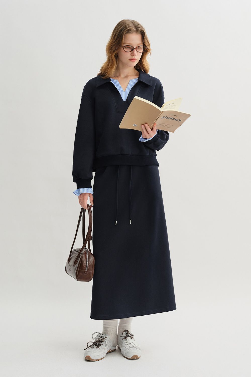 Side view of woman in navy blue pullover with light blue striped collar and cuffs, styled with matching skirt