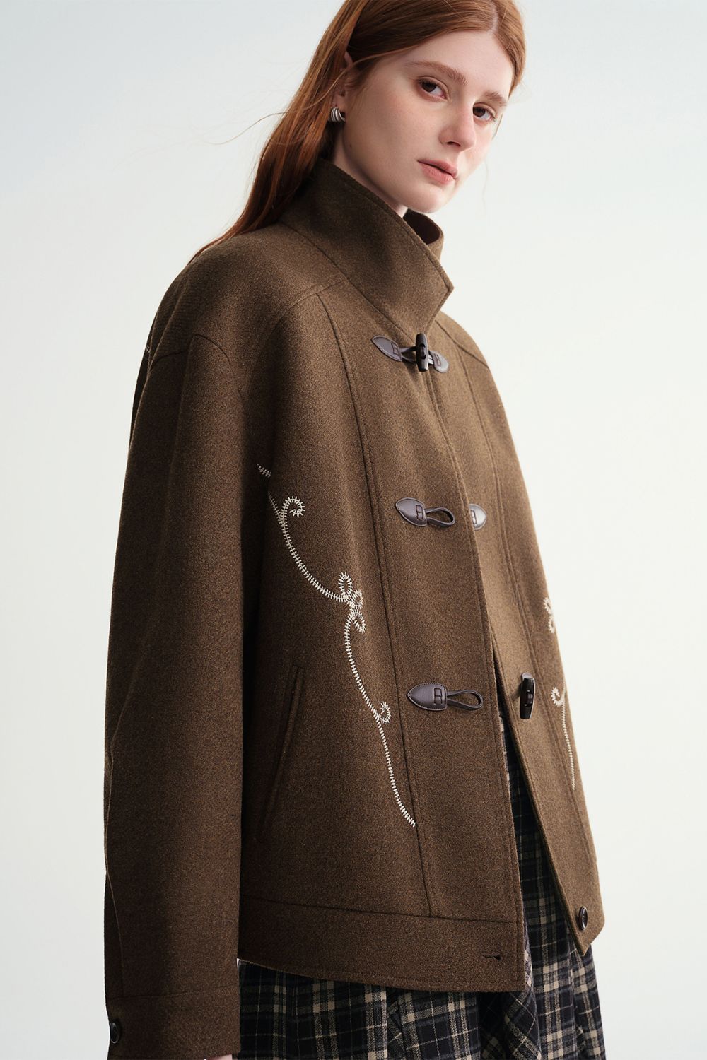 Side view of model in brown toggle jacket with plaid skirt