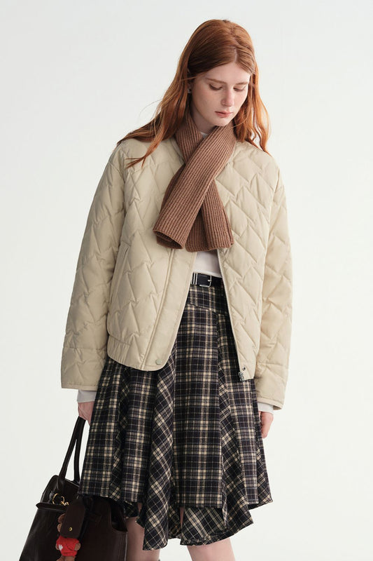 Model wearing a beige quilted jacket styled with a brown scarf and plaid skirt