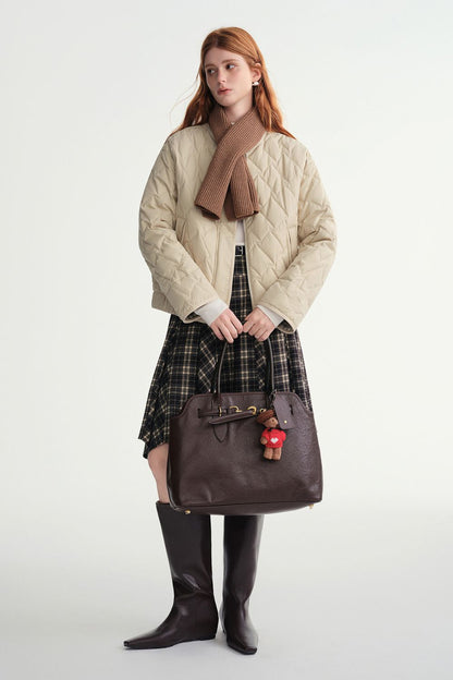 Model wearing a beige quilted jacket styled with a brown scarf and plaid skirt and brown handbag