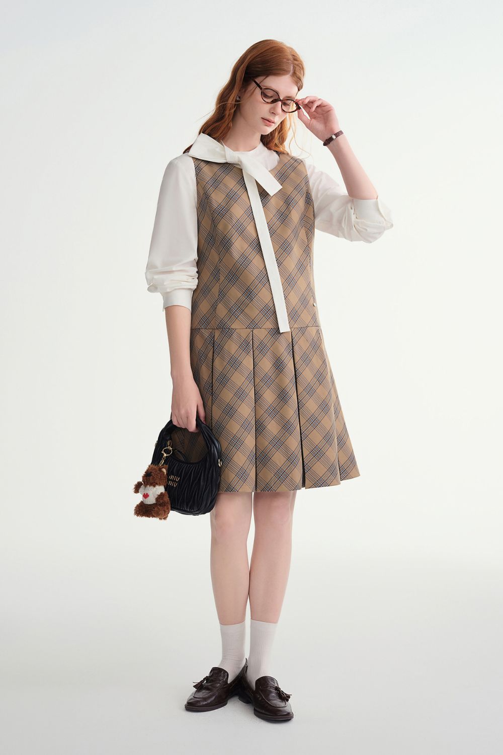 Angled view of model holding a black handbag while wearing plaid dress and blouse