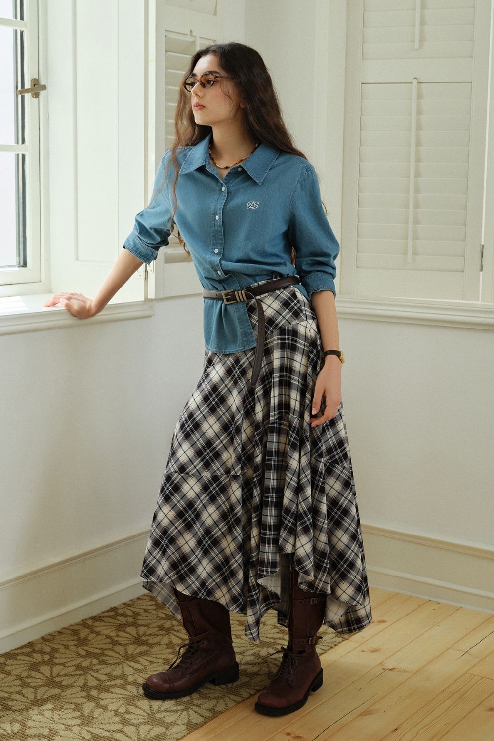 Model in a denim shirt wearing the plaid asymmetrical skirt indoors