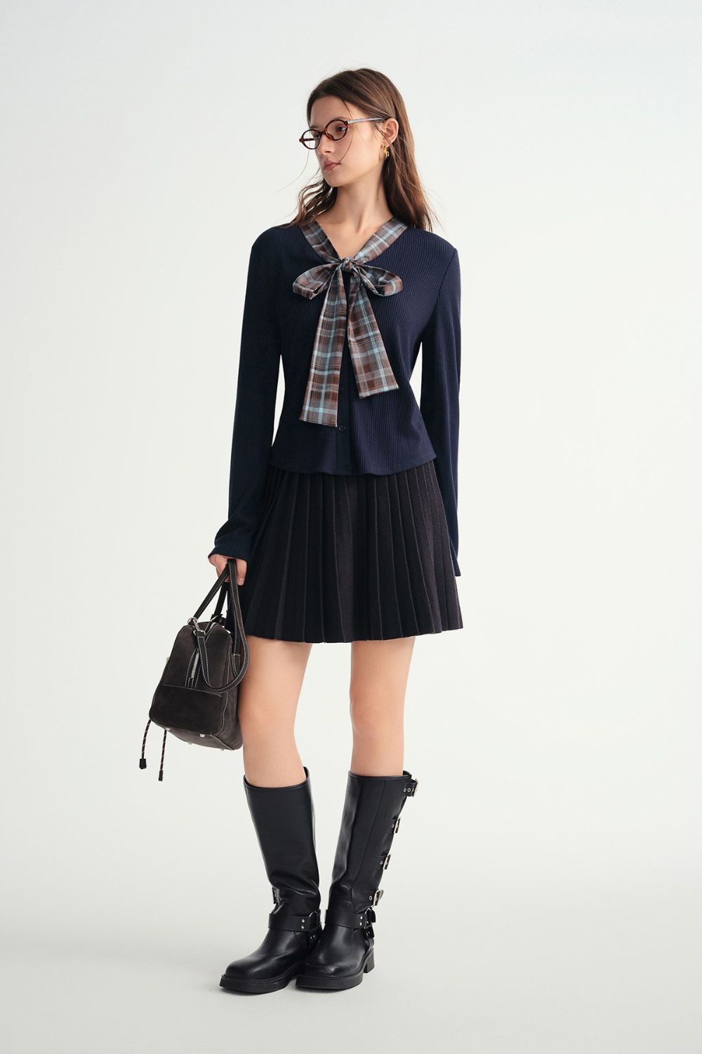 Angled view of model in navy blue pleated skirt and plaid bow blouse