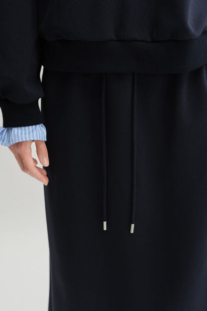 Close-up of sleeve and waistband details of navy blue pullover with light blue striped shirt cuffs