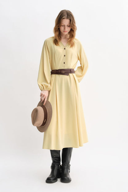 Angled standing view of yellow belted dress with hat accessory