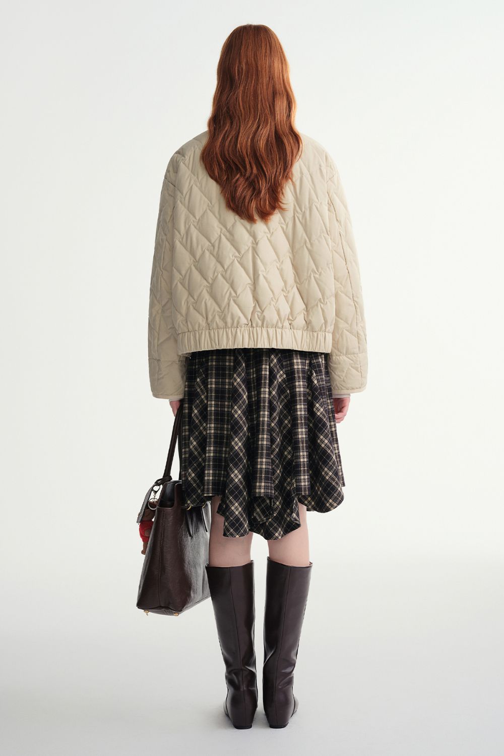 Back view of beige quilted jacket styled with a plaid skirt