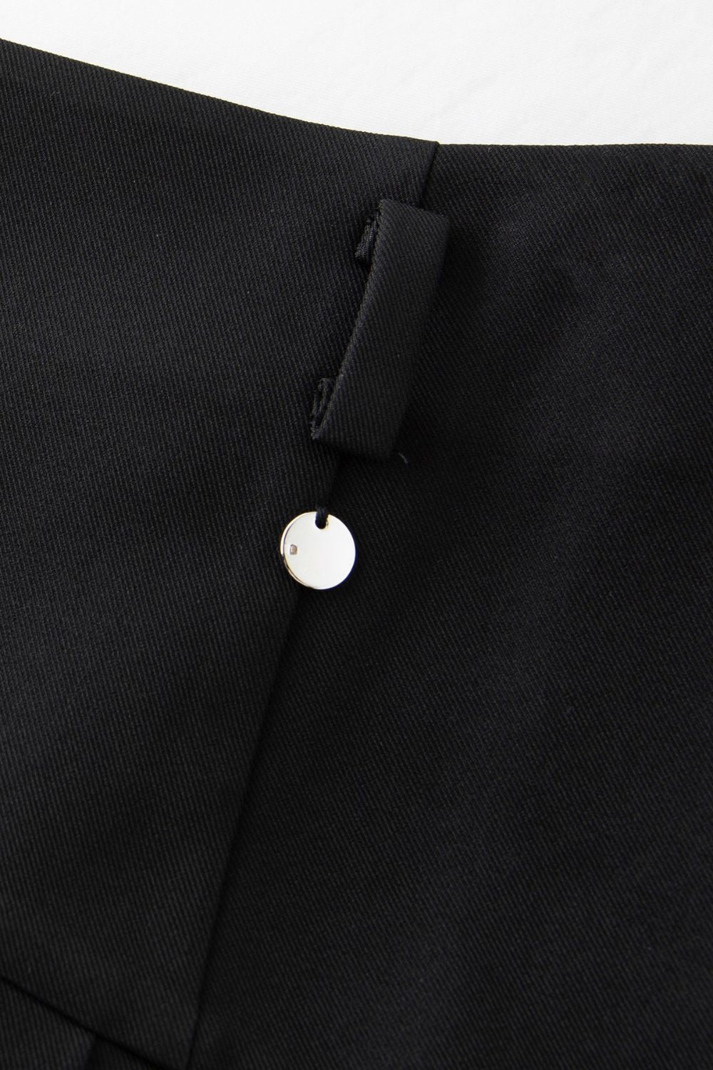 Close-up of button and waistband detail on pleated skirt