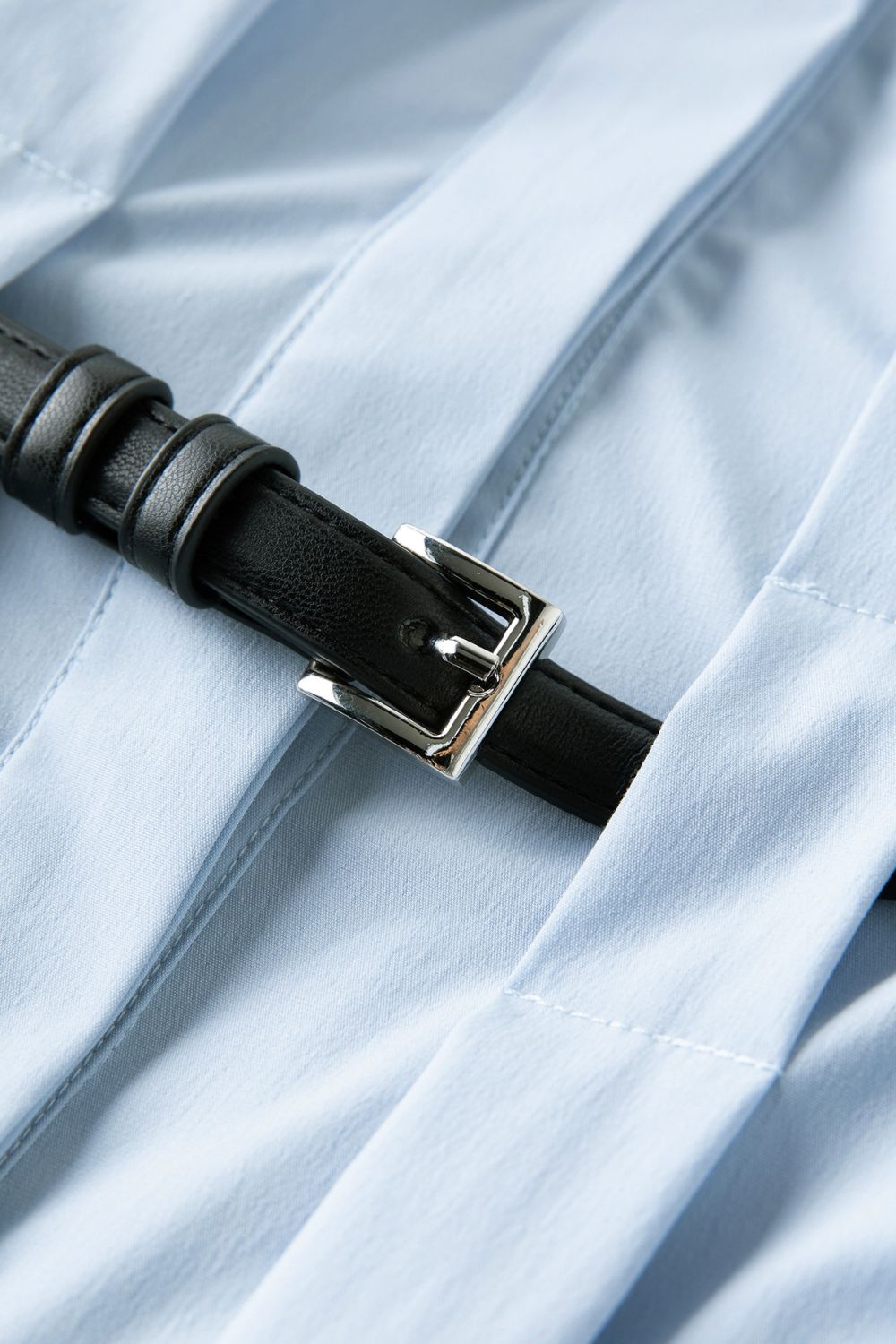 Close-up of black belt buckle detail on light blue dress