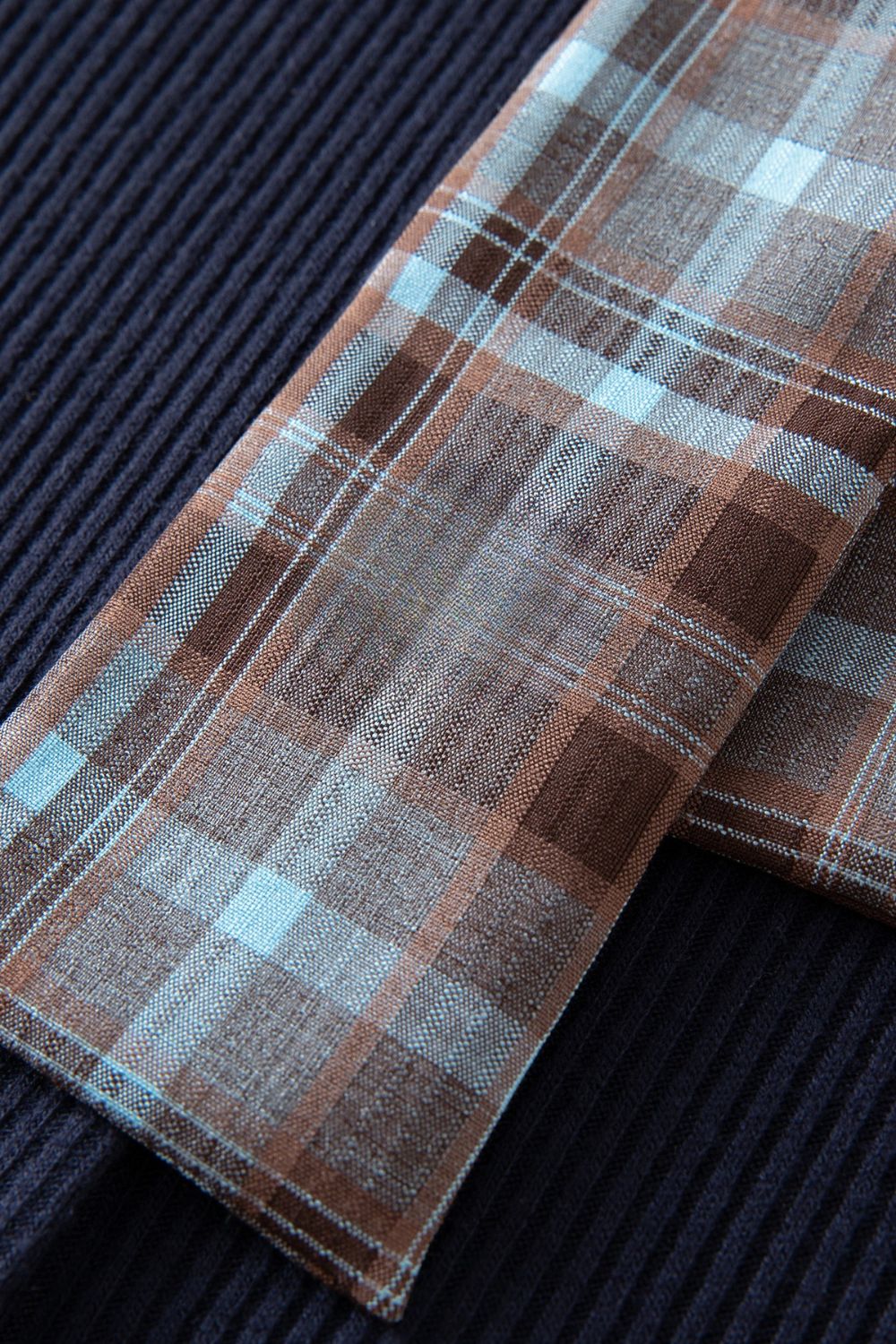 Close-up of navy blue ribbed fabric with plaid bow tie end