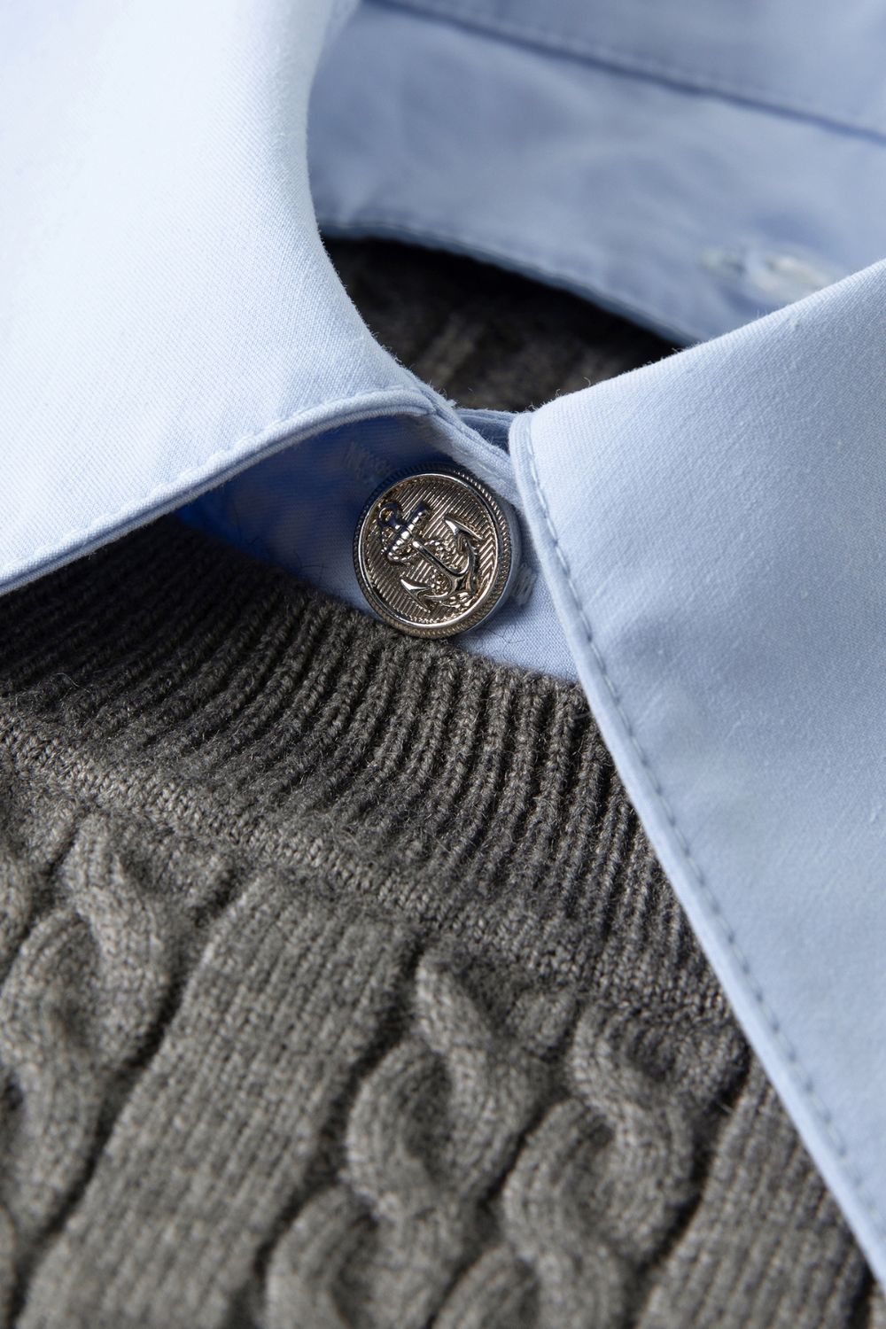 Close-up of blue collared shirt under gray sweater with button detail