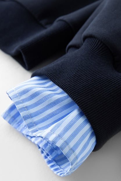Close-up of light blue striped shirt cuff under navy blue pullover sleeve