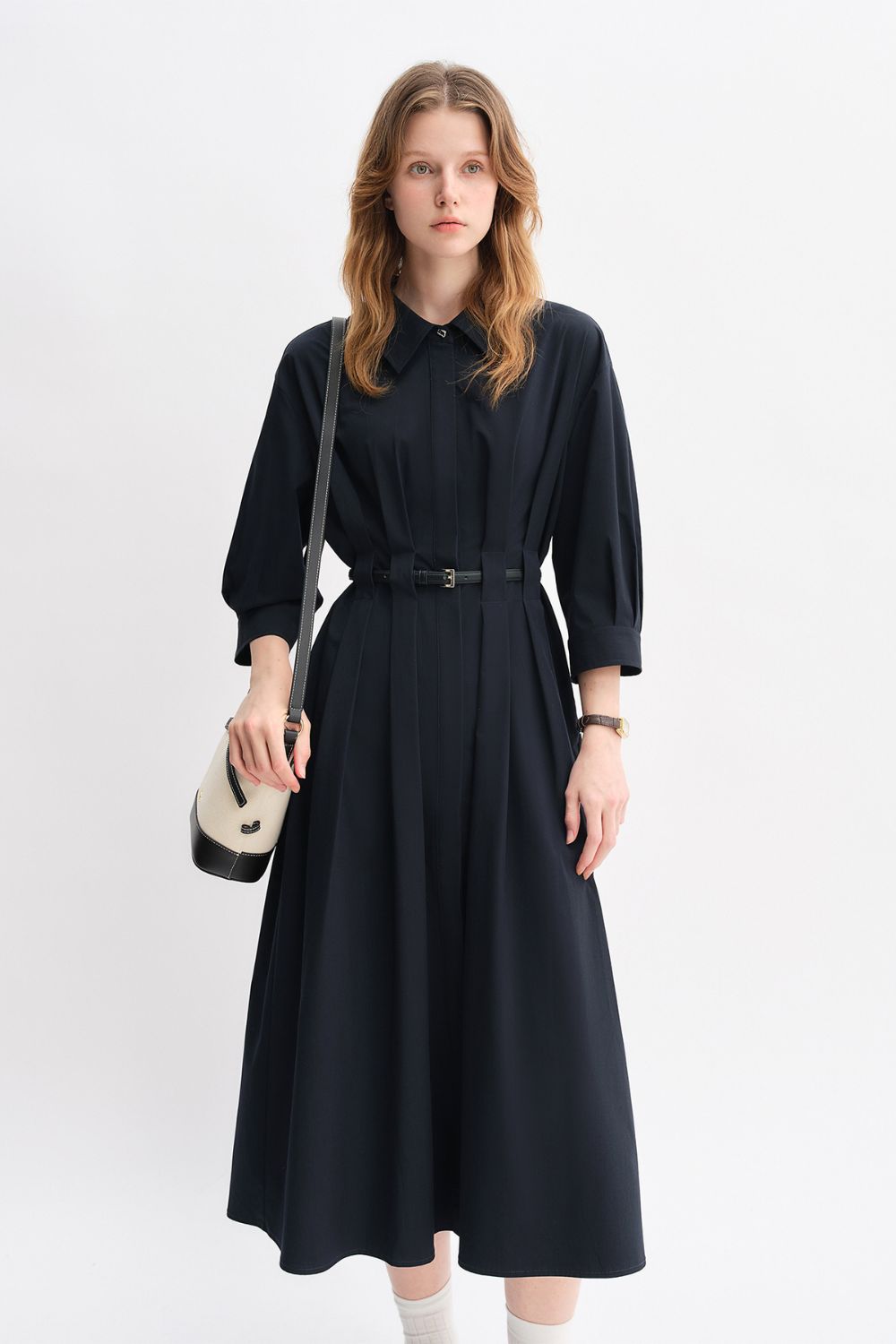 Model in a black belted midi dress with long sleeves and a small handbag