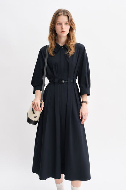 Model in a black belted midi dress with long sleeves and a small handbag