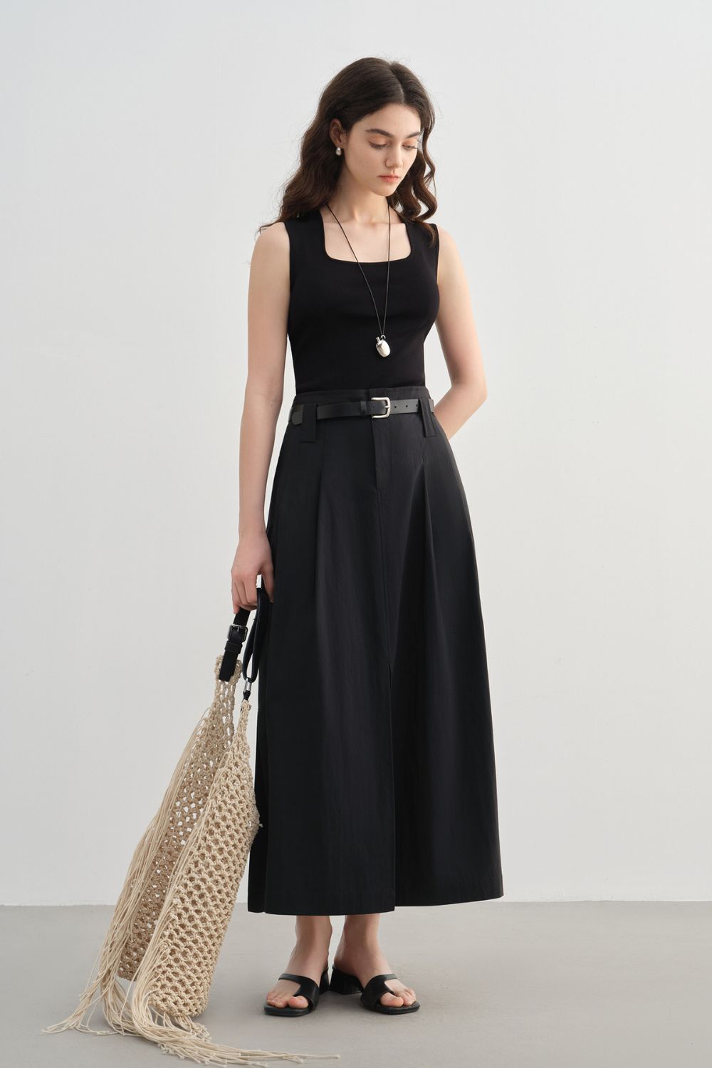 Model in black sleeveless top wearing black midi skirt with front slit