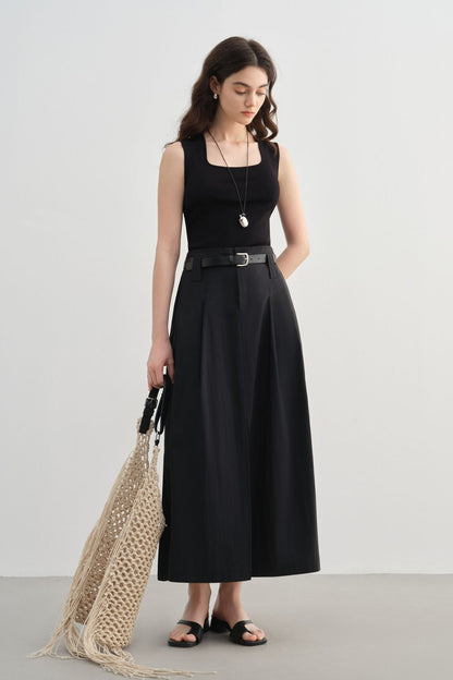 Model in black sleeveless top wearing black midi skirt with front slit