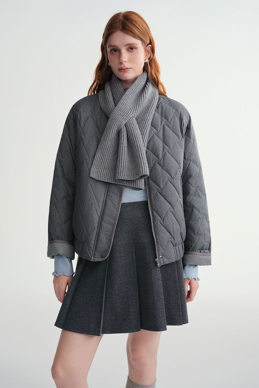 Model wearing a gray quilted jacket with a dark gray skirt and gray scarf