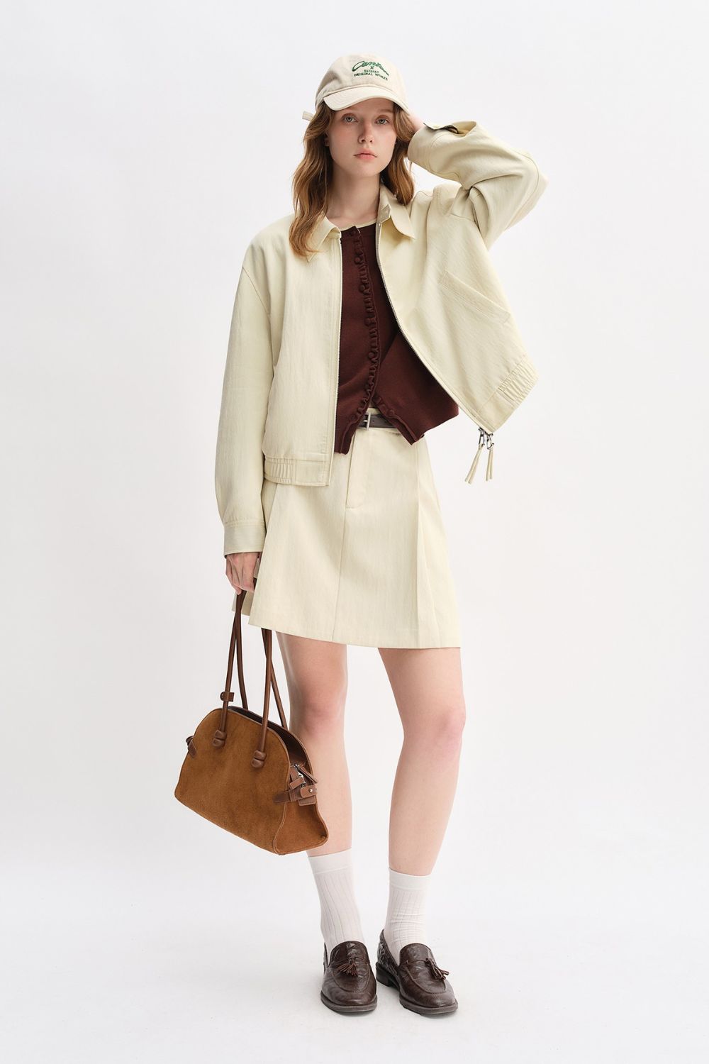 Model in cream jacket and skirt set holding brown handbag